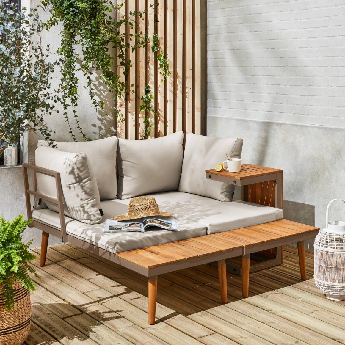 Canapé d'extérieur gris avec coussins beiges, table basse en bois, plante et lanterne en rotin