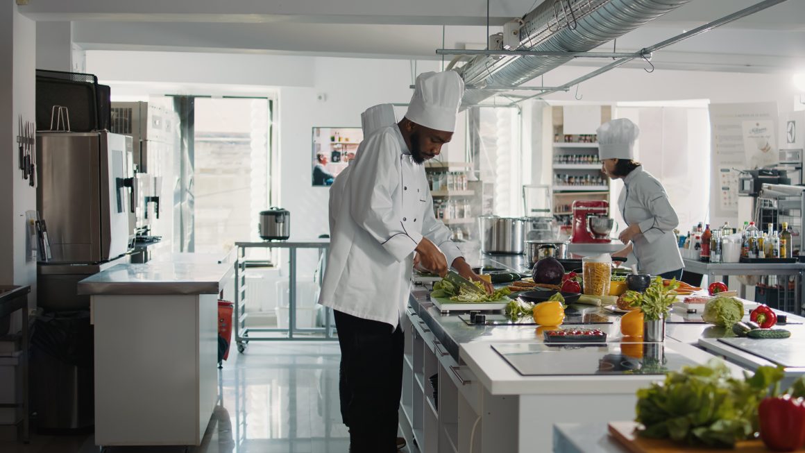 Deux chefs cuisiniers préparant des plats sur un plan de travail dans une cuisine professionnelle entièrement équipée