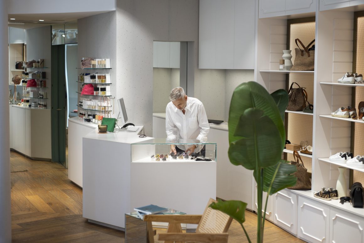 Vendeur organise des accessoires dans une boutique incluant étagères de sacs, chaussures et présentoirs soignés