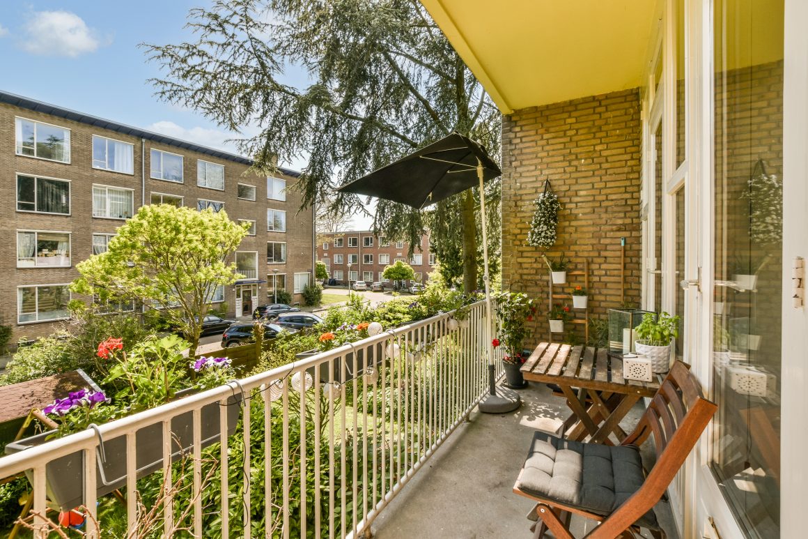 Aménagement balcon 10m2 avec chaises en bois, table, plantes et parasol noir