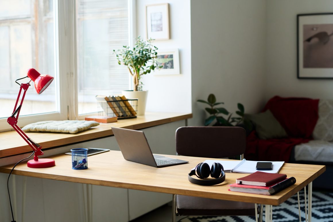 Bureau près d’une fenêtre incluant ordinateur portable, lampe rouge, casque, carnets et plante