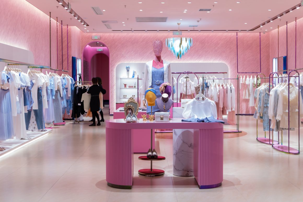 Boutique moderne : décor rose pastel, présentoir central, vêtements, mannequins et éclairage doux