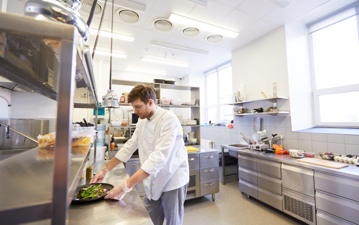 Chef en blouse blanche dressant une assiette dans une cuisine professionnelle moderne