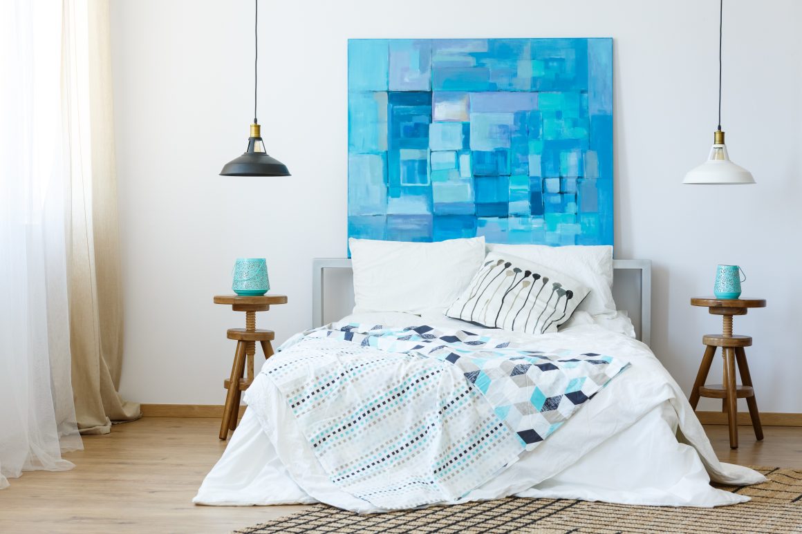 Chambre incluant lit blanc, toile bleue abstraite, tables en bois, tapis et suspensions