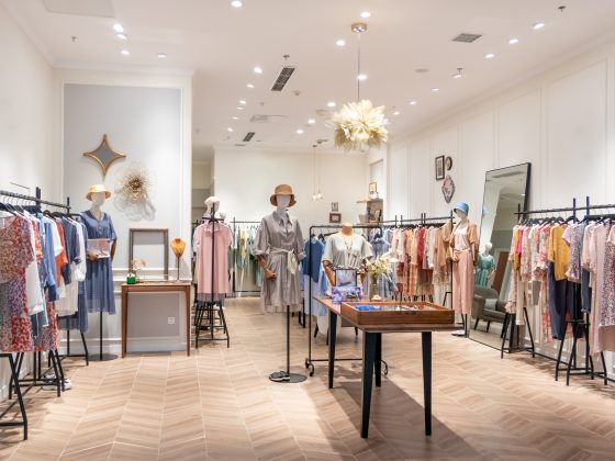 Boutique aménagée avec sol chevrons bois, mannequins, vêtements colorés, miroir, déco murale et luminaires