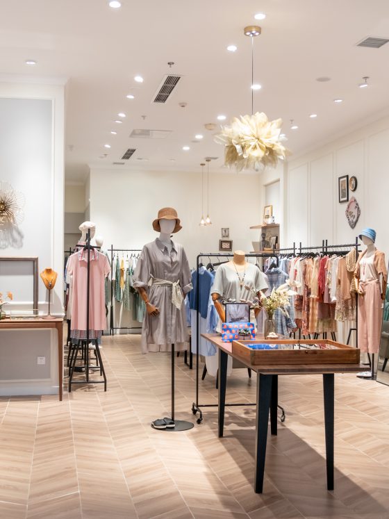 Boutique aménagée avec sol chevrons bois, mannequins, vêtements colorés, miroir, déco murale et luminaires