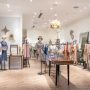 Boutique aménagée avec sol chevrons bois, mannequins, vêtements colorés, miroir, déco murale et luminaires
