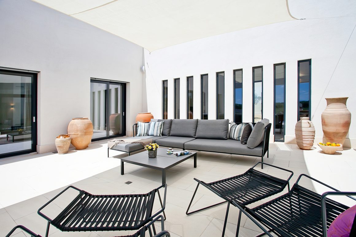 Terrasse moderne incluant canapé gris, fauteuils noirs, table basse et grandes jarres en terre cuite