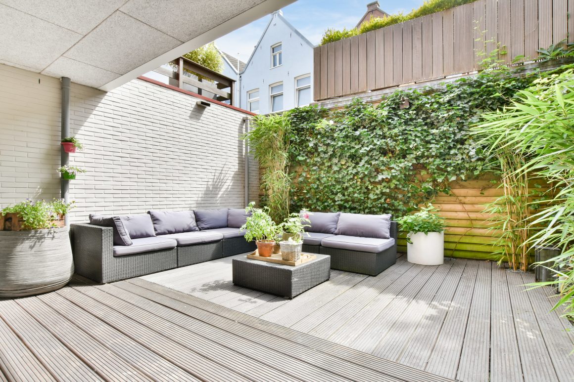 Terrasse contemporaine incluant canapés gris en rotin, table basse, plantes grimpantes et lattes de bois