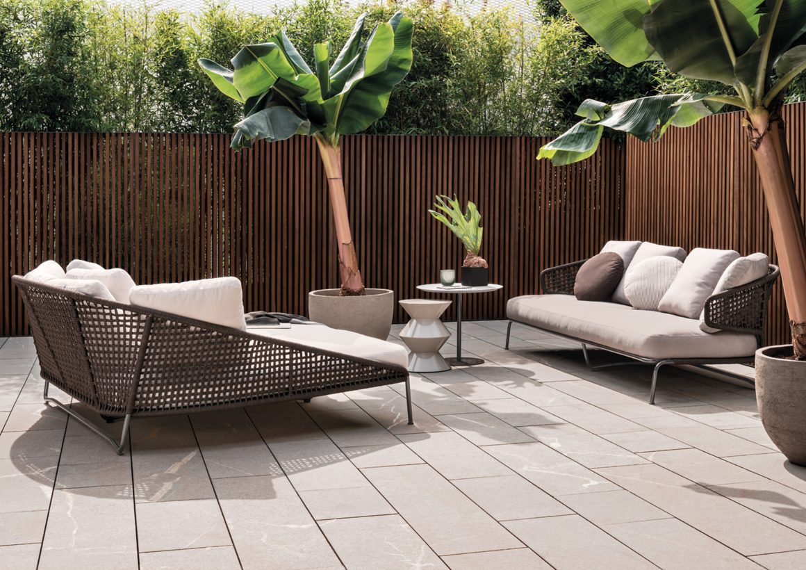 Coin extérieur élégant : canapés tressés, plantes tropicales, table basse et clôture en bois
