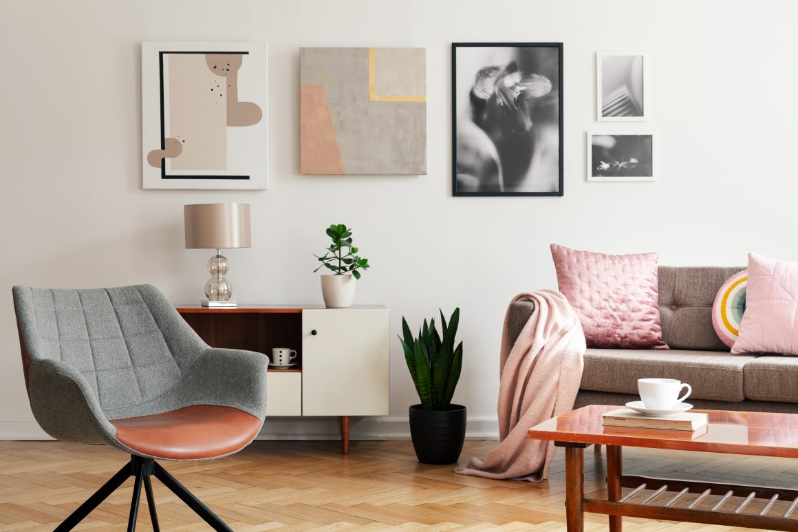 Salon lumineux incluant sofa rose, fauteuil gris, table en bois, plantes et tableaux muraux