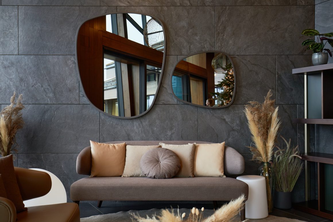 Salon incluant canapé marron avec coussins beiges, miroirs organiques et plantes séchées décoratives
