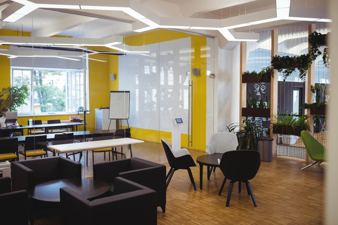 Espace de coworking avec murs jaunes, plantes, tables de réunion, tables basses, chaises et fauteuils