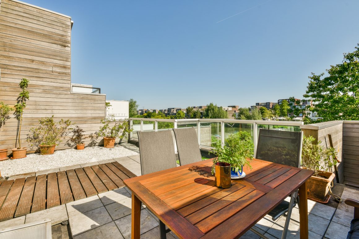 Terrasse ensoleillée incluant table en bois, chaises, plantes en pots et balustrade en verre