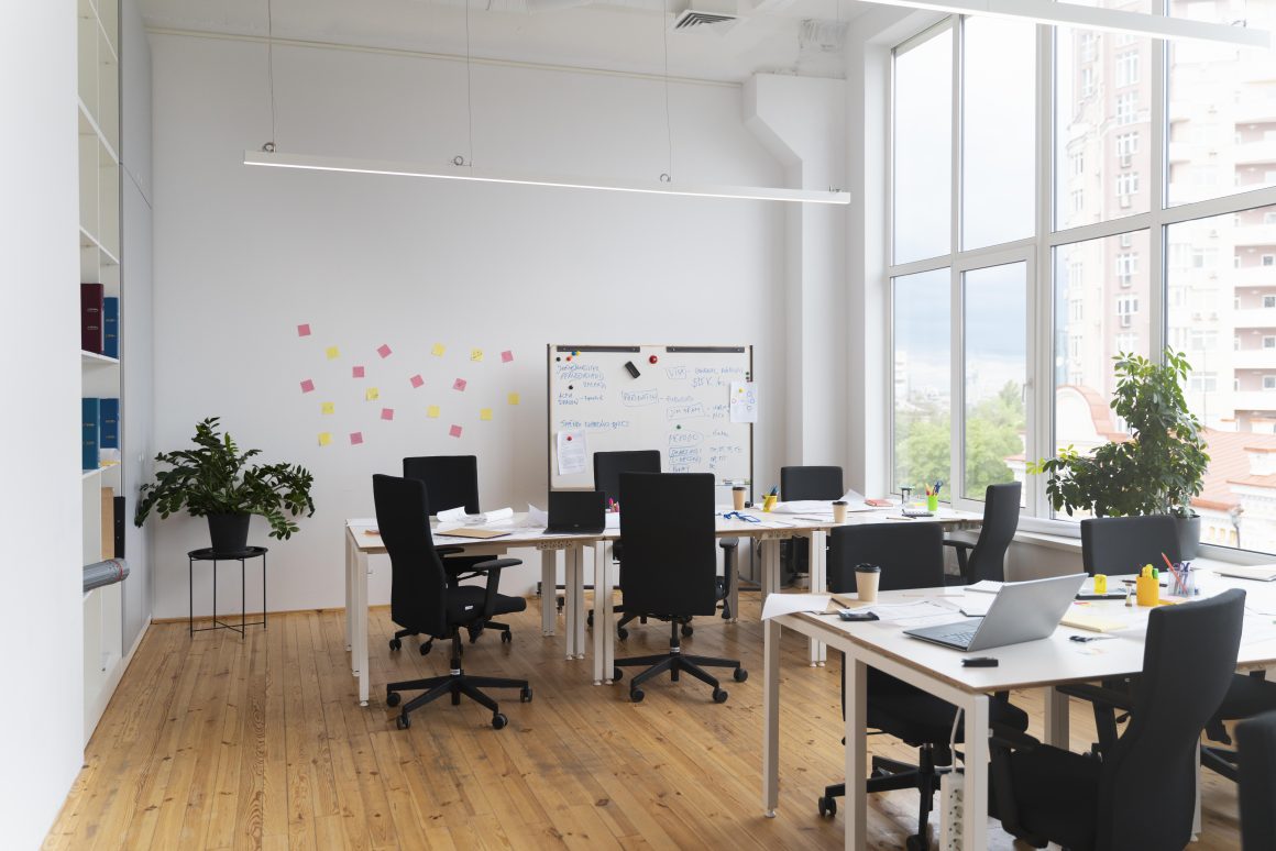 Bureau professionnel incluant grandes fenêtres, plantes, chaises noires, bureaux blancs et tableau