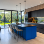 Cuisine moderne incluant îlot bleu, surfaces noires et bois, luminaires suspendus et grandes baies vitrées