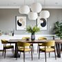 Grande table à manger en bois avec chaises jaunes, luminaires blancs, buffet blanc et plantes
