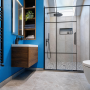 Salle de bain avec peinture bleu lumineux, douche vitrée, meuble lavabo flottant en bois et sol en carrelage gris