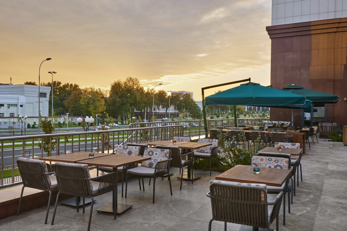 Terrasse de café chic au coucher du soleil incluant tables en bois, fauteuils et parasols verts