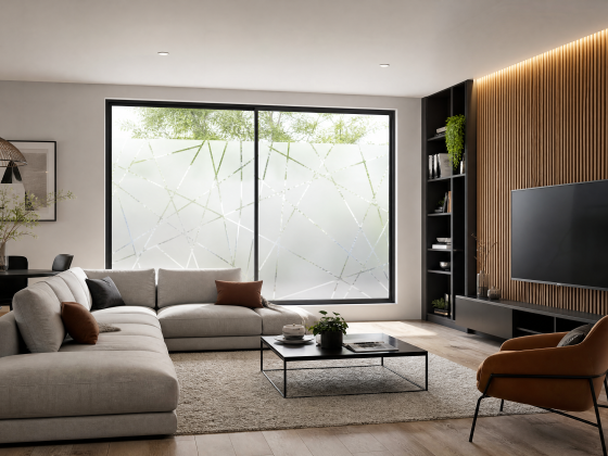 Canapé d'angle, fauteuil, table basse, plantes, TV murale et baie vitrée habillée avec film dépoli à motifs géométriques