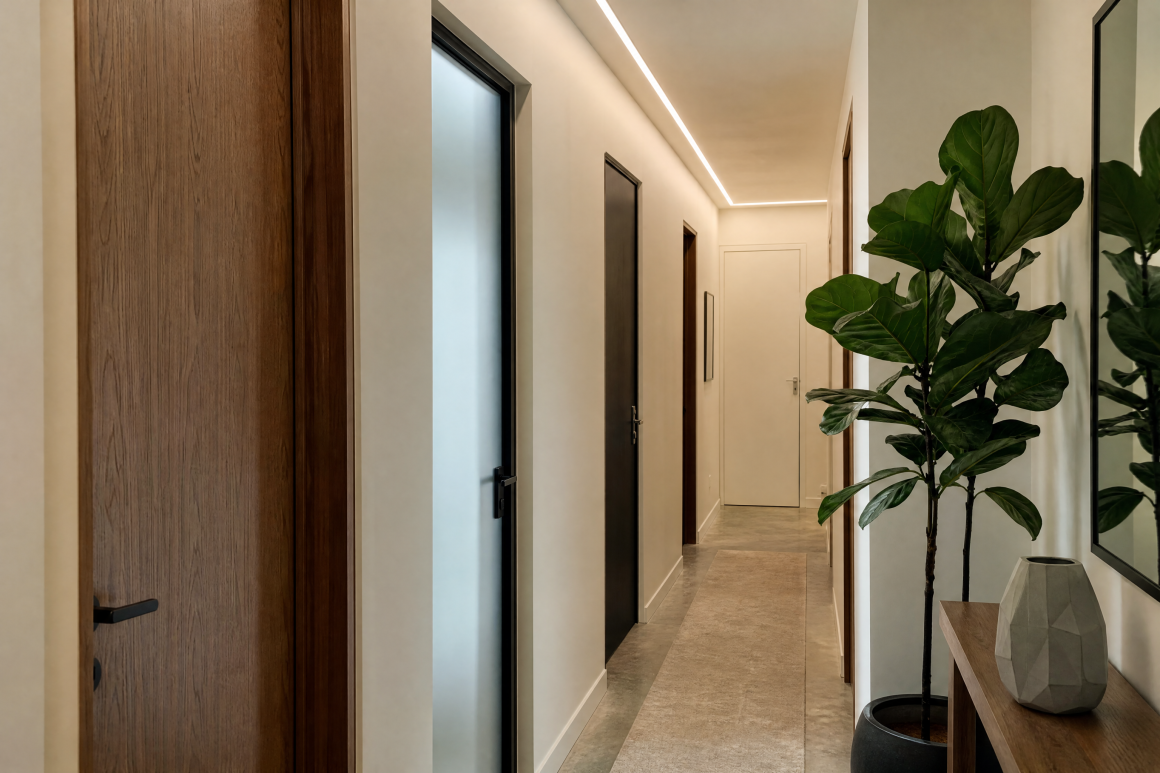 Couloir avec portes en bois foncé, éclairage LED au plafond, plante et console minimaliste