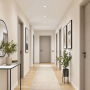 Couloir avec murs crème, portes grises, sol en bois clair, tapis, plantes, miroir et cadres