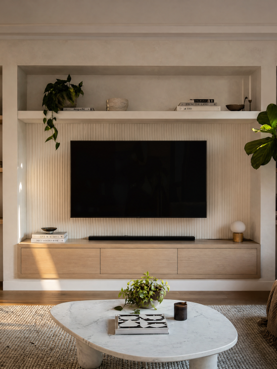 Salon aux tons neutres : TV encastrée dans un mur avec étagères, plantes, canapé et table basse en marbre