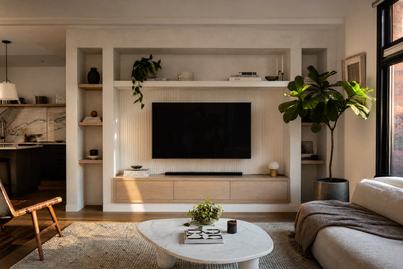 Salon aux tons neutres : TV encastrée dans un mur avec étagères, plantes, canapé et table basse en marbre