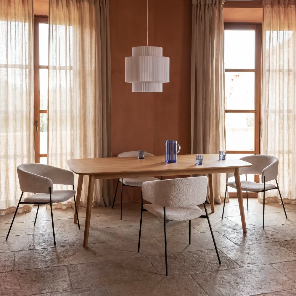 Table à manger en bois clair avec chaises rembourrées crème, suspension et grandes fenêtres voilées