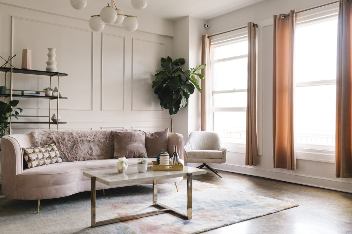 Canapé rose poudré avec fauteuil crème, table basse, grande plante, rideaux terracotta et tapis doux