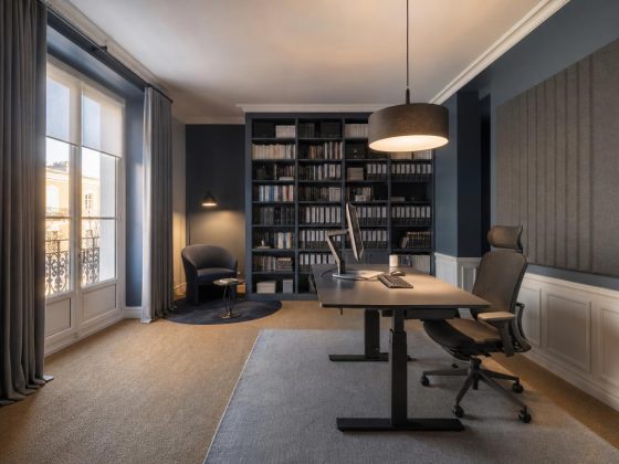 Bureau avec mobilier gris et noir, bibliothèque remplie, panneau acoustique mural et grande fenêtre avec rideaux