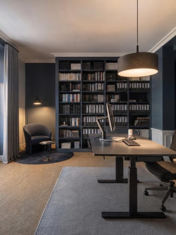 Bureau avec mobilier gris et noir, bibliothèque remplie, panneau acoustique mural et grande fenêtre avec rideaux