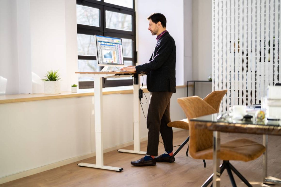 Homme travaillant debout à un bureau réglable dans un espace lumineux incluant chaises et table