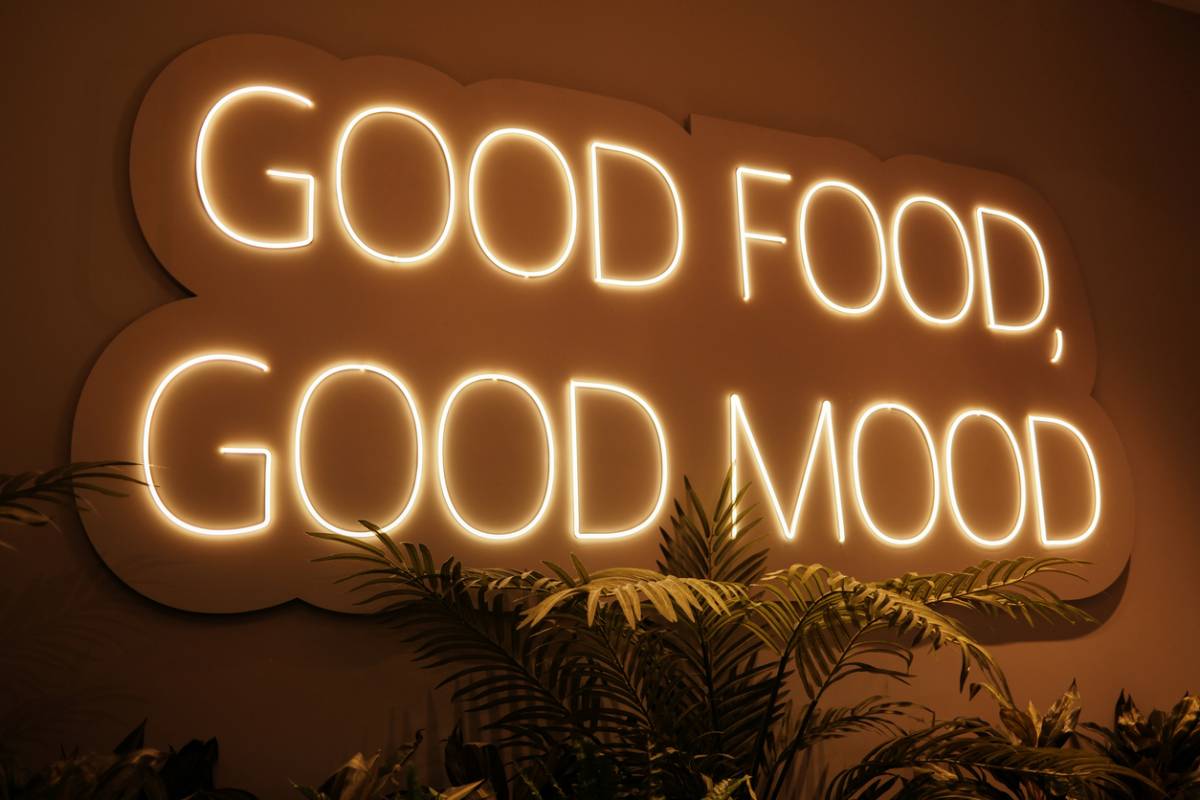 Panneau mural lumineux diffusant la phrase Good food good mood au-dessus de plantes vertes