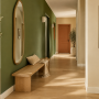 Passage avec mur vert olive, long banc en chêne et porte terracotta au fond